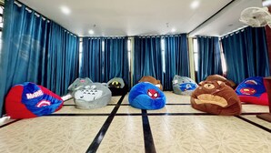 A room with a tiled floor, blue curtains, and several bean bags with superhero designs. - Paradise Hostel  (Vang Vieng)