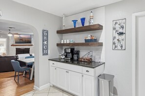 Una cocina con armarios blancos, una zona de café y vistas al salón.