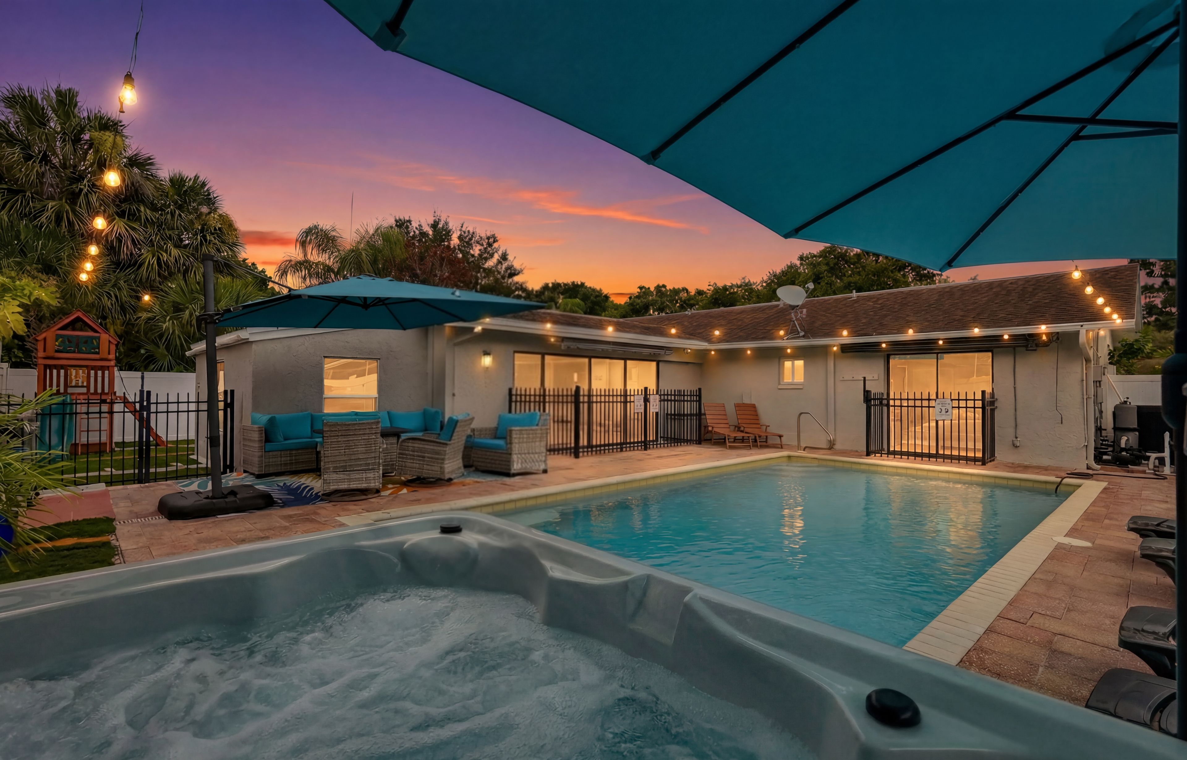A swimming pool with a hot tub, outdoor seating, and string lights.