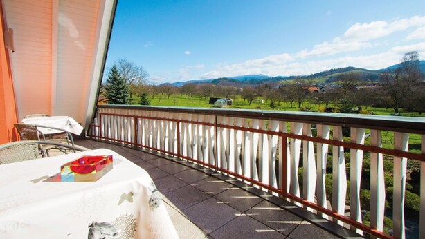 Een balkon met uitzicht op een groen landschap en bergen.