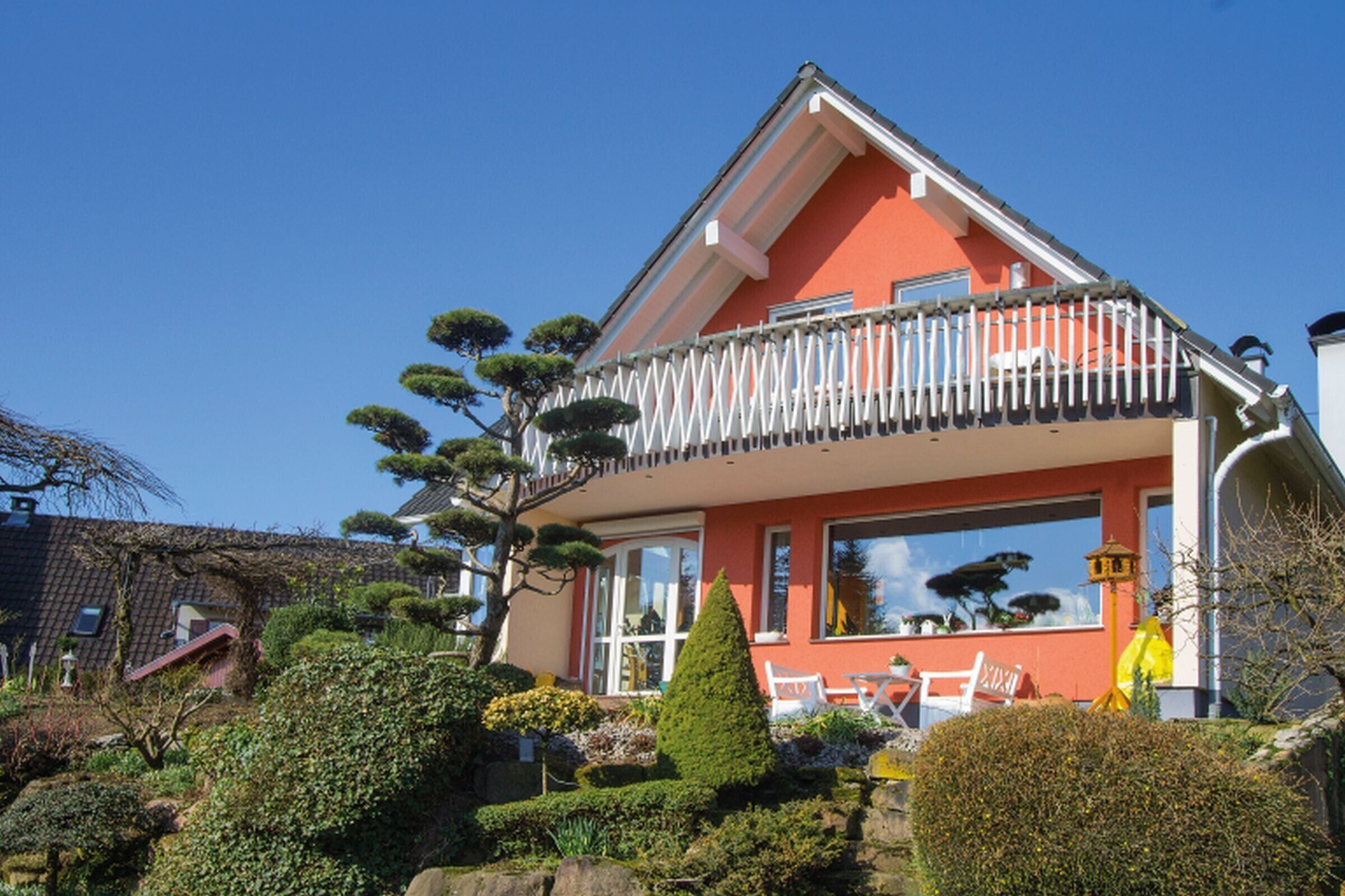 Ein Haus mit Balkon, ein Garten mit verschiedenen Pflanzen und ein klarer, blauer Himmel.