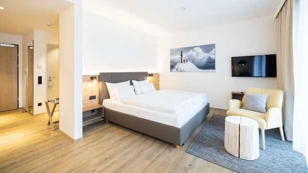 Una habitación de hotel moderna con una cama grande, televisión, una silla y un cuadro en la pared.