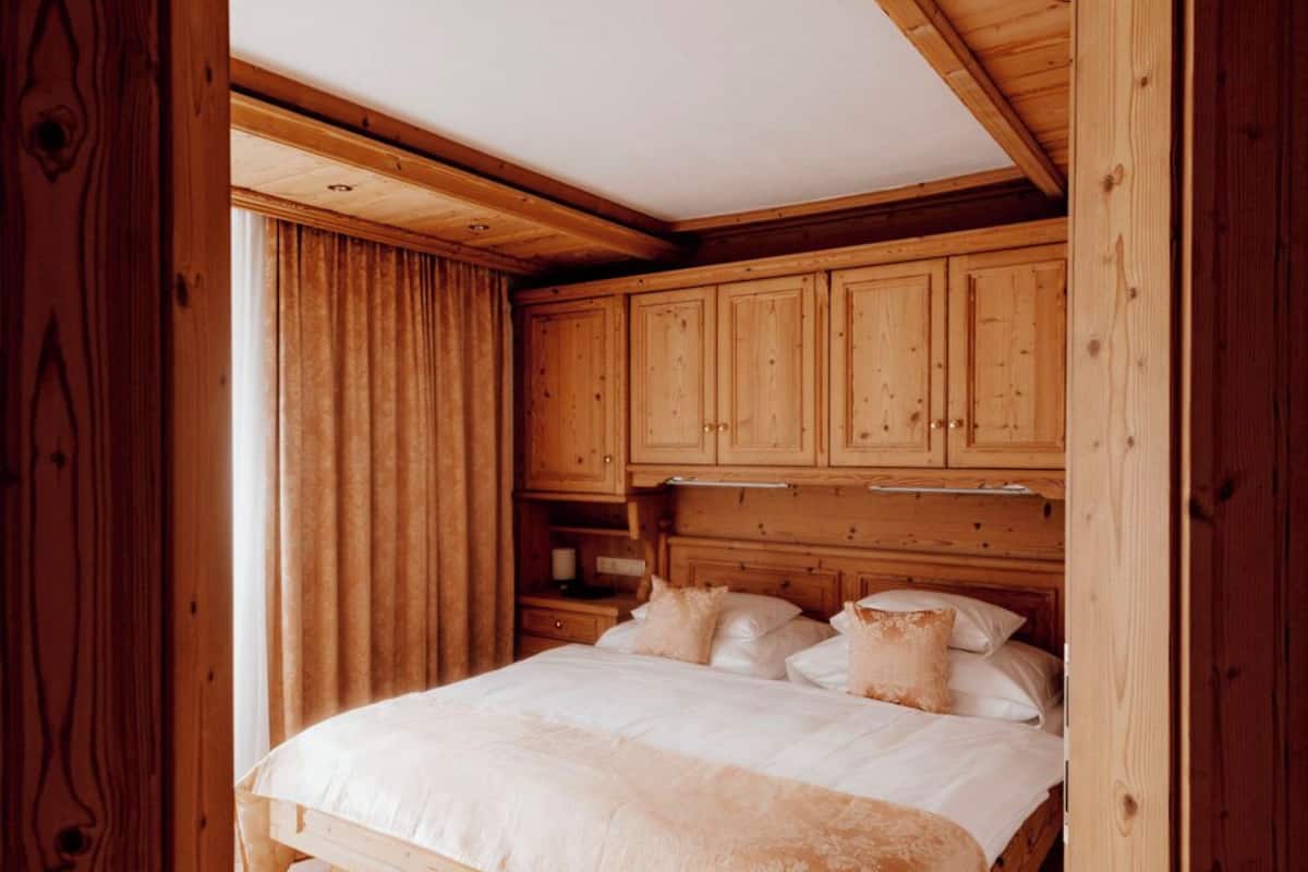 Un dormitorio de madera con cama, cortinas y suelo de baldosas.