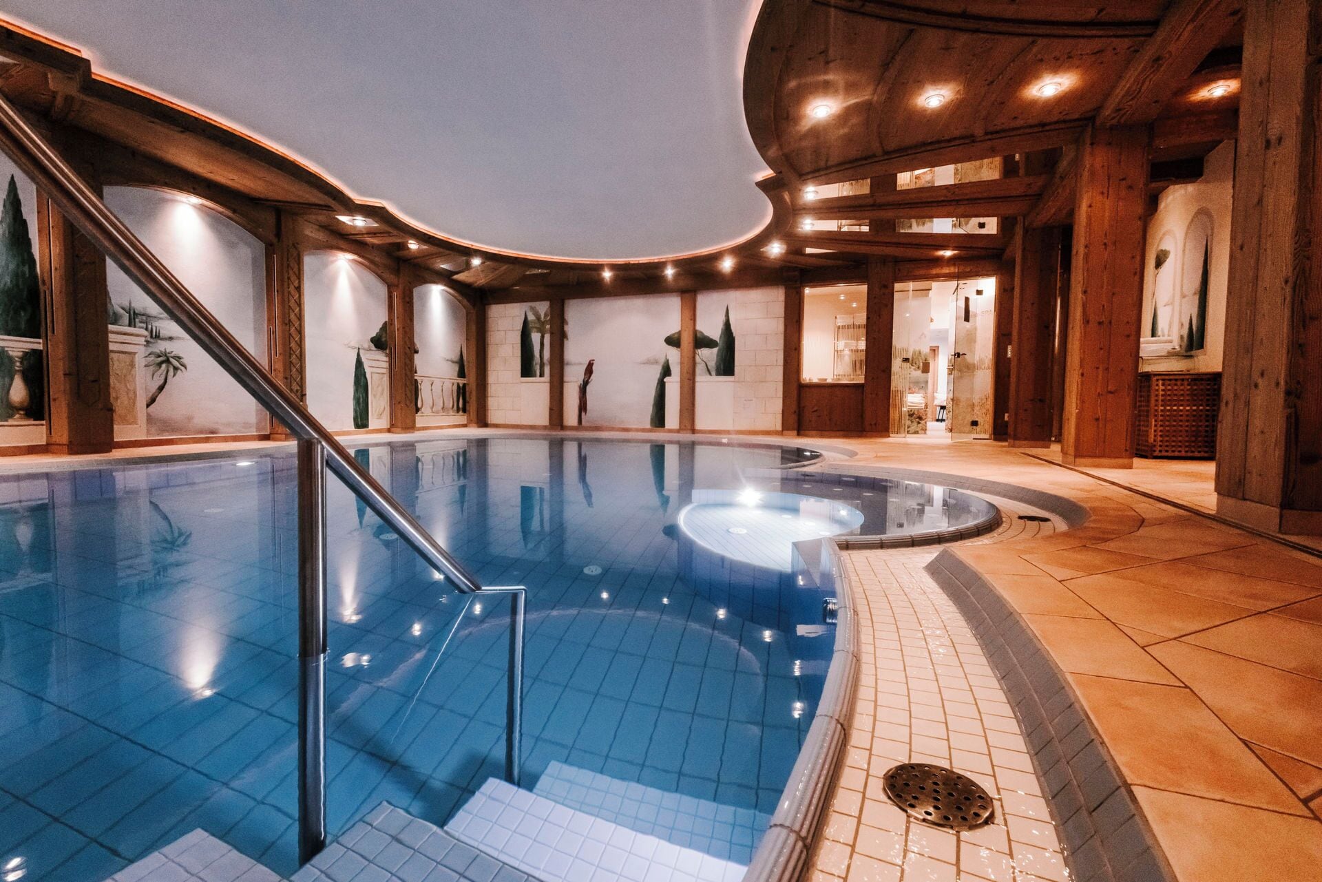 Una piscina interior con vistas claras al área de la piscina, una escalera que conduce al nivel superior y una recepción visible a través de las puertas de cristal.