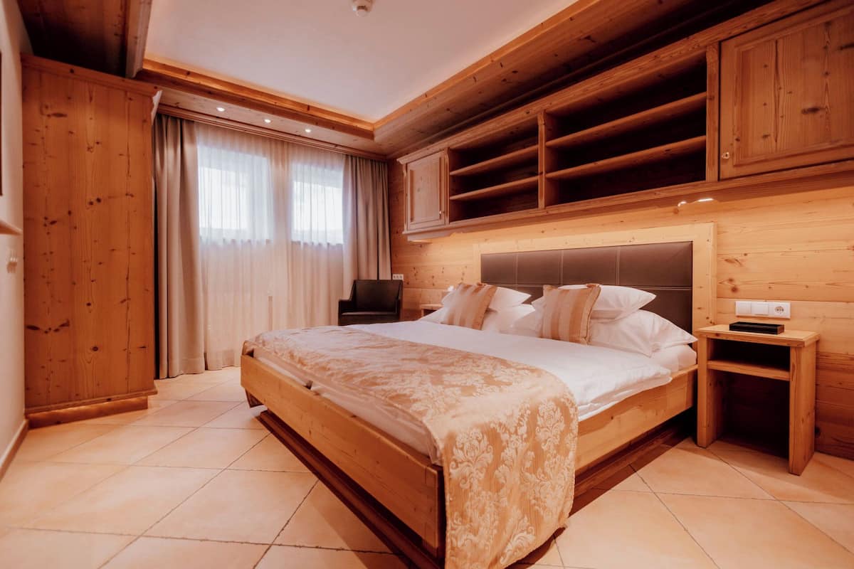 Un dormitorio de madera con una cama grande, estanterías empotradas, una mesita de noche y una ventana con cortinas.