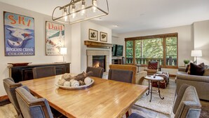 Amplia sala de estar con una mesa de comedor de madera, asientos cómodos, una chimenea y grandes ventanales con vistas al exterior.