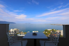 A balcony with a table and chairs overlooking a body of water and cityscape. - Hill Suites (Vlore)