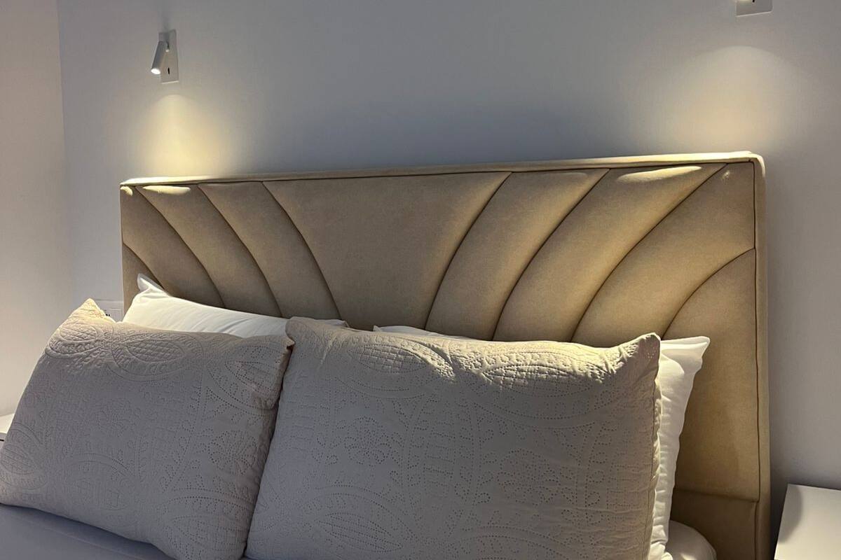 Uma cama com cabeceira estofada, duas almofadas e uma mesa de cabeceira com interruptor de luz.