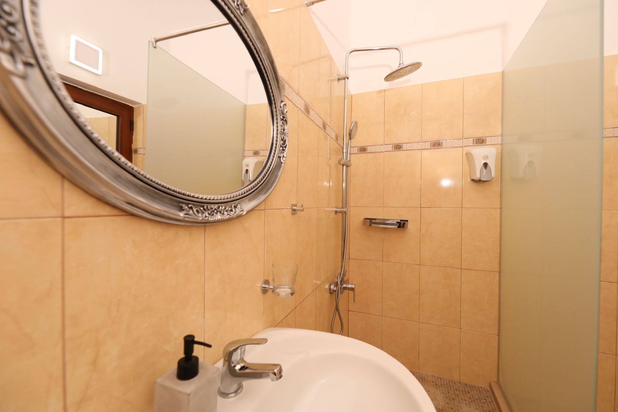Une salle de bain avec un lavabo blanc, un miroir et une douche fermée par une paroi de verre.