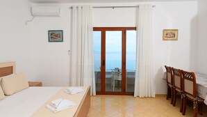 A hotel room with a bed, a dining table with chairs, a balcony with a view of the sea, and two framed pictures on the walls. - Hill Suites (Vlore)
