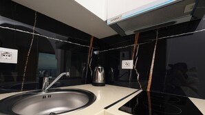 A modern kitchen with a stainless steel sink, black and white backsplash, and a black stove. - Hill Suites (Vlore)