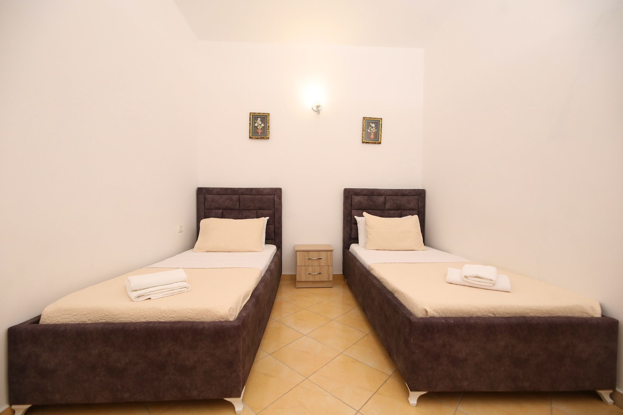 A room with two beds, a small bedside table, and a wall-mounted light fixture.