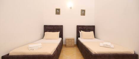 A room with two beds, a small bedside table, and a wall-mounted light fixture.