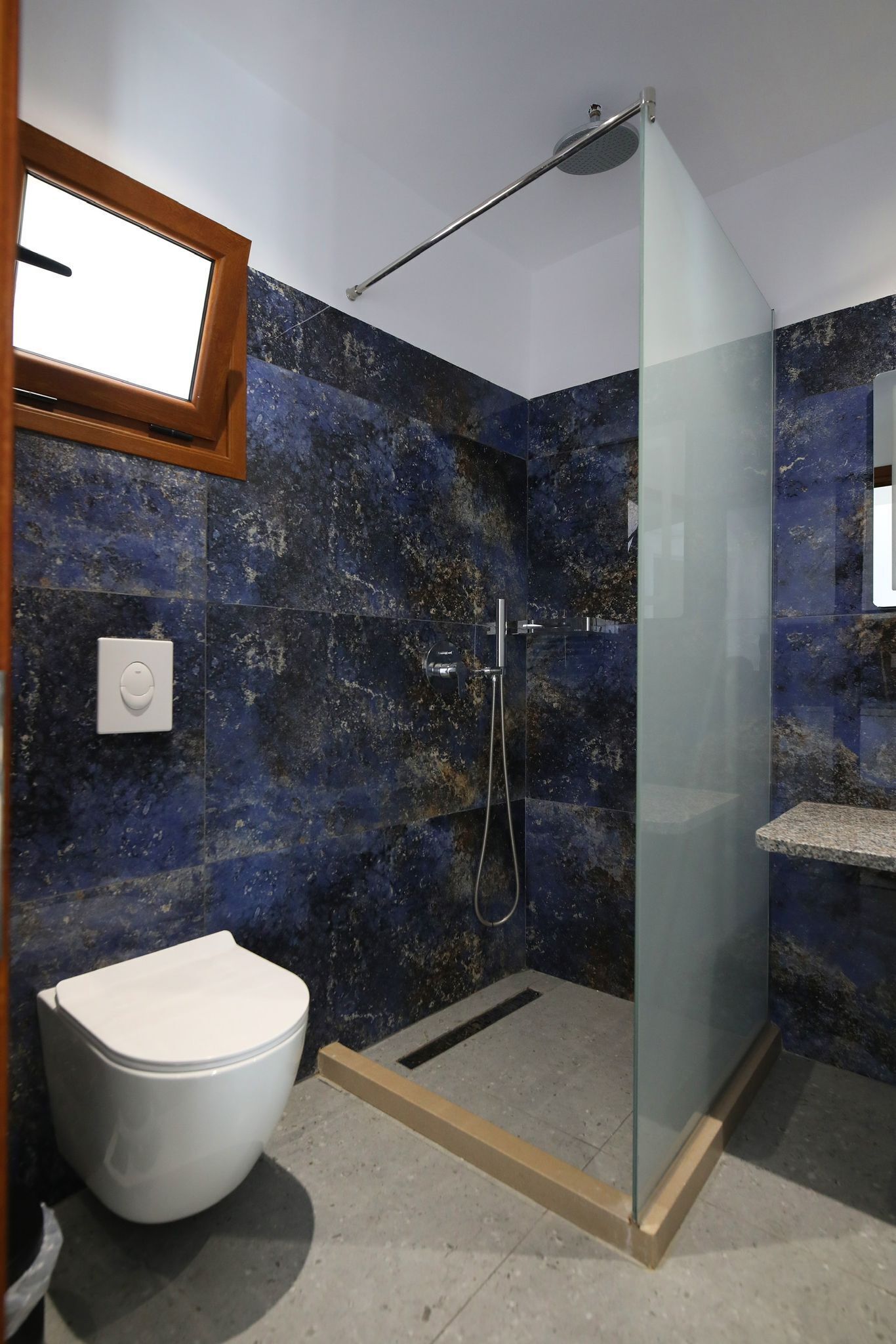 Un baño con ducha envuelta en cristal, inodoro blanco y pared de mármol.