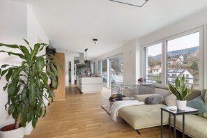 A modern living room with a sofa, a coffee table, a large potted plant, and a view of a balcony.