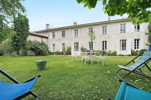 A building with a garden, outdoor furniture, and a trash bin.