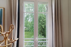 A room with a large window, a wicker chair, and a view of a garden.