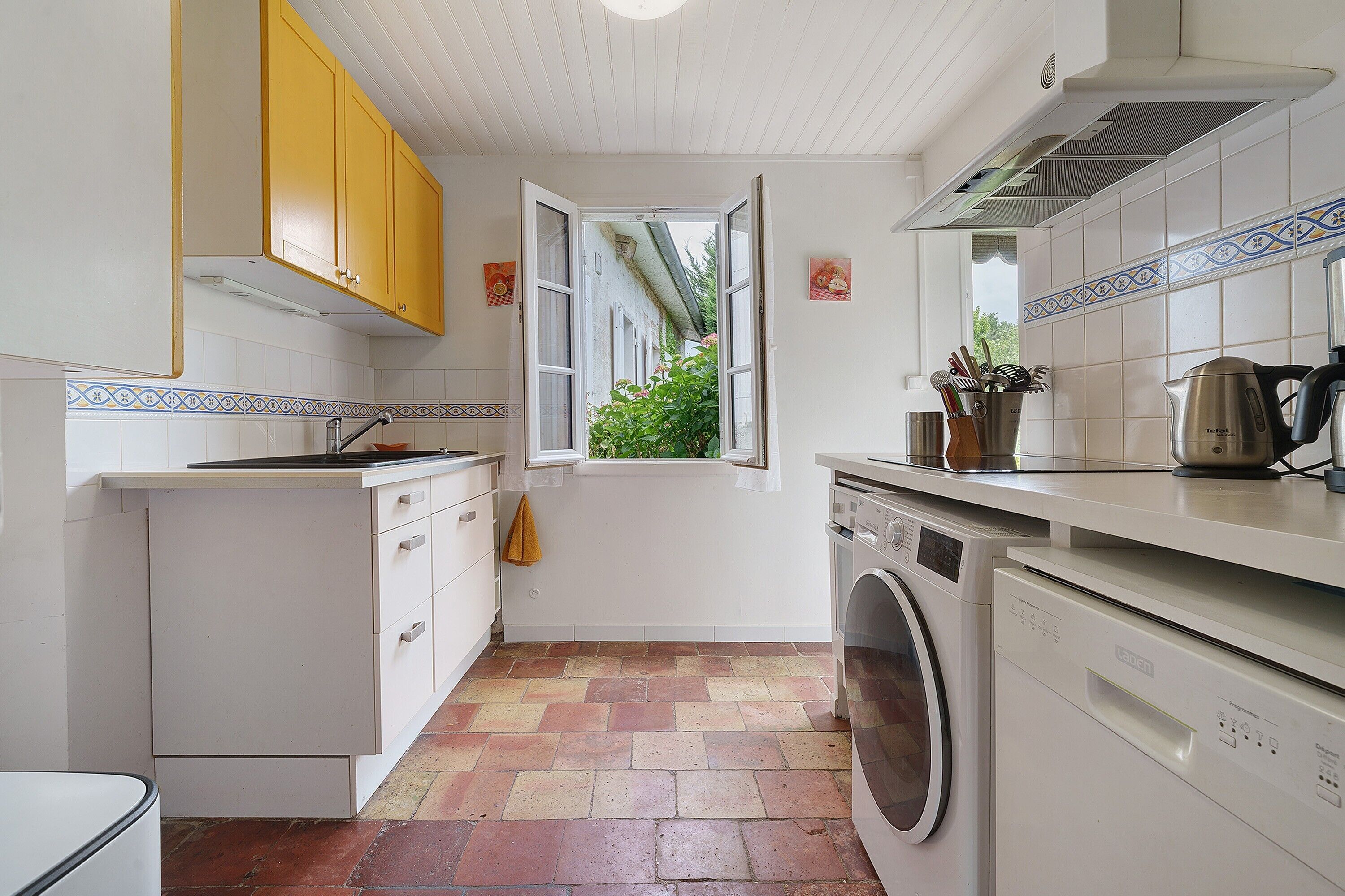 A compact kitchen with white cabinets, a washing machine, and a window with a view of greenery.