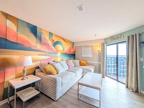 A modern living room with a sofa, a coffee table, a lamp, and a large abstract painting on the wall. - 2BR Tower Ocean View | Myrtle Beach Resort RT0513 (Myrtle Beach)