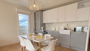 A modern kitchen with white cabinets, a marble backsplash, and a dining area with a glass table and white chairs. - Le Penthouse Pesaro C - Concert Celine DION (Nanterre)