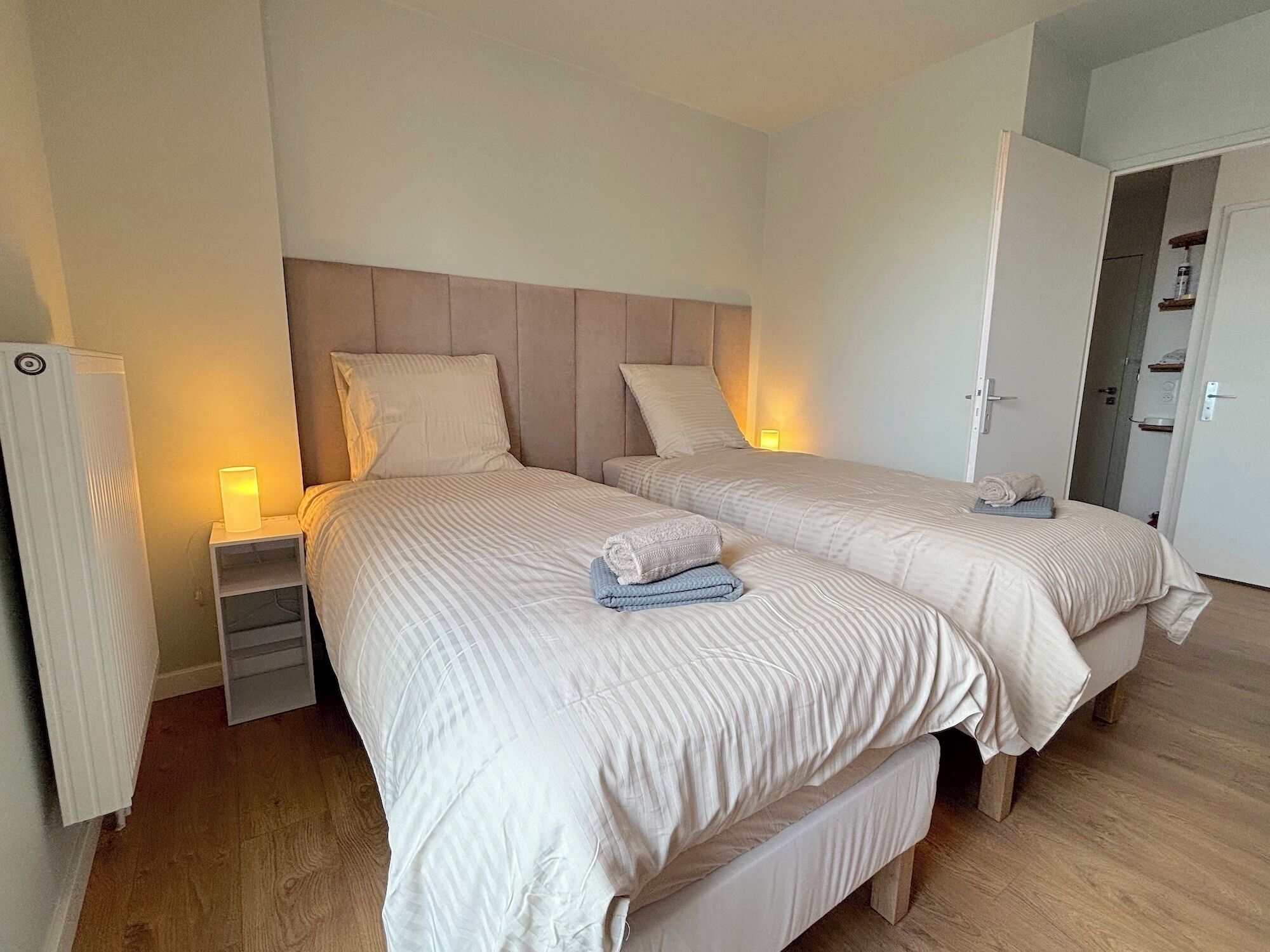 A hotel room with two beds, each with a headboard, bedside tables, and lamps.