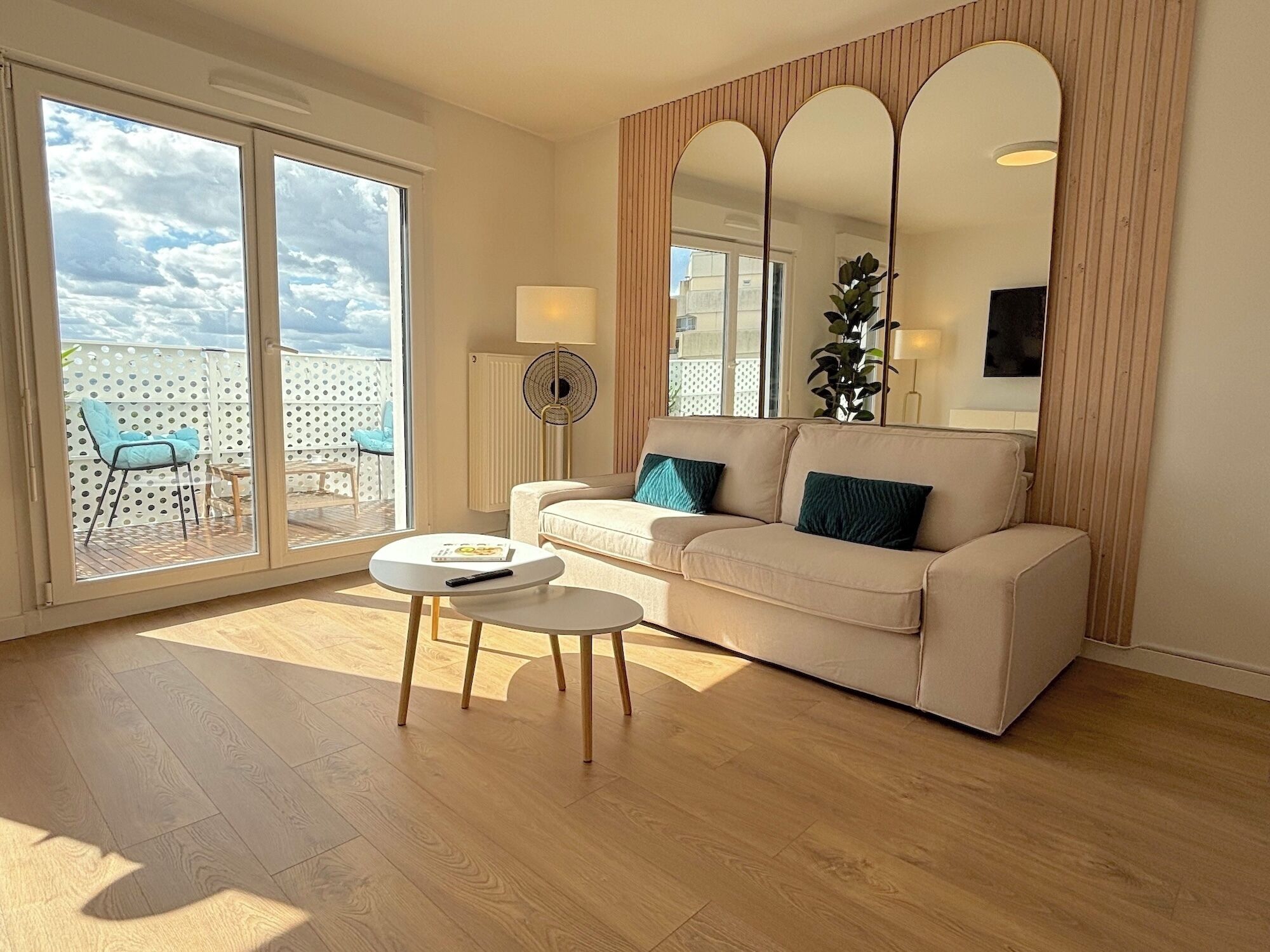 Een moderne woonkamer met een beige bank, een klein rond tafeltje en een grote glazen schuindeur die leidt naar een terras met een blauwe stoel.