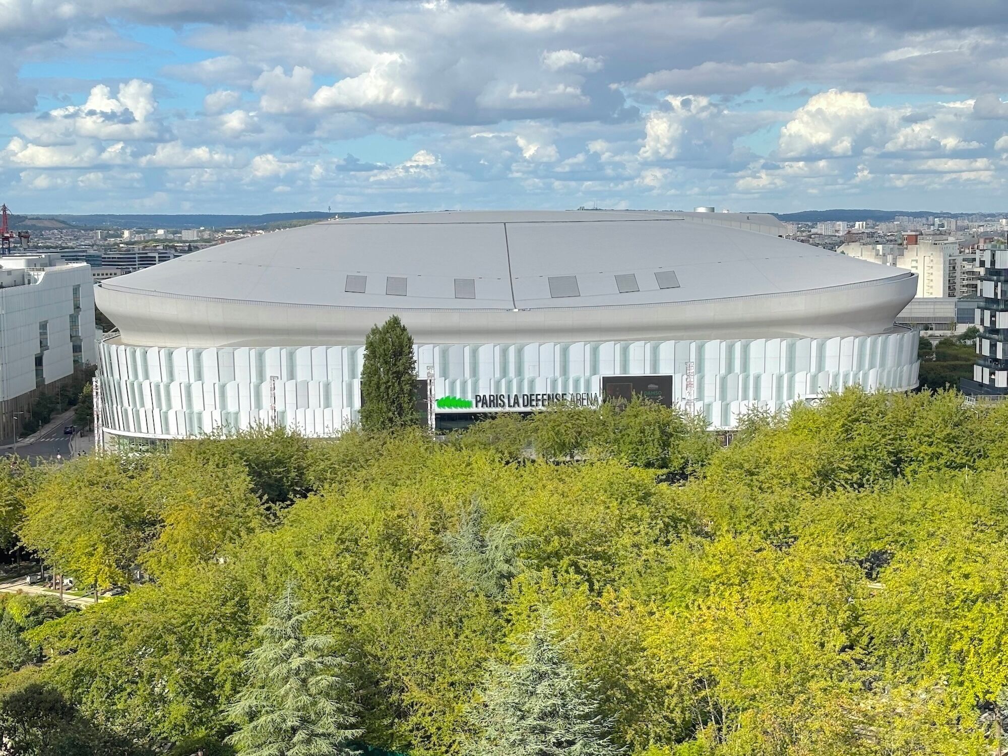 Een modern, rond gebouw met een plat dak en een bord waarop staat: PARIS LA DEFENSE ARENA.