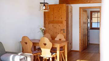 Ein Esszimmer mit Holztisch, Stühlen, einer Couch und einer Pendelleuchte. Die Wände und der Boden sind ebenfalls aus Holz.