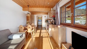 A cozy interior with a wooden ceiling, a sofa, a dining area, and a kitchen with large windows. - Apartment 'Hirtebube' with Shared Garden, Balcony, and Wi-Fi (Lenzkirch)