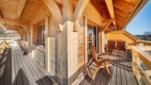 Una terraza de madera con una mesa y sillas de madera, una barandilla y vistas al exterior.