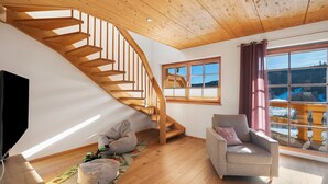 Un interior moderno con una escalera de madera, un ventanal con vistas, un sofá y un televisor.