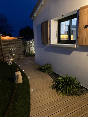 Een modern huis met een houten terras, een stenen muur en een kleine tuin met planten.
