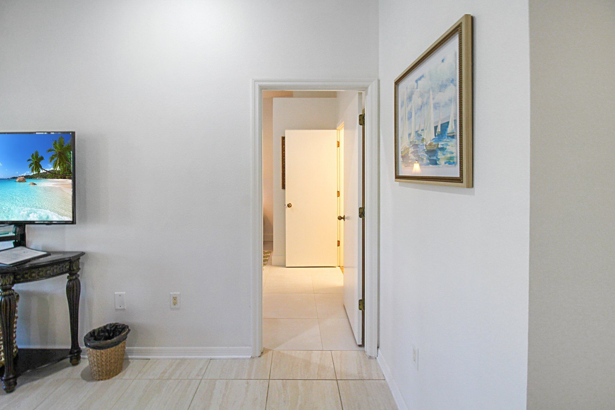 Um corredor com televisão à esquerda, um quadro emoldurado à direita e uma porta que dá para outro quarto.