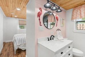 Une chambre avec un lit, une coiffeuse blanche avec un lavabo, et un mur rose décoré de motifs de flamants roses.