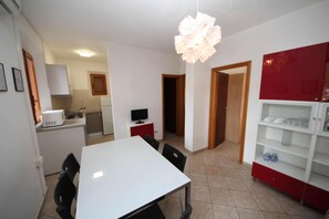 A compact kitchen with white cabinets, a dining table, and chairs. There is a red cabinet with glassware and a white cabinet with a microwave. - Welcoming Apartment Steps From the Beach (Rosolina)