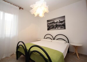 A bedroom with a bed, a bedside table, a chair, a hanging light fixture, and a wall-mounted picture. - Welcoming Apartment Steps From the Beach (Rosolina)