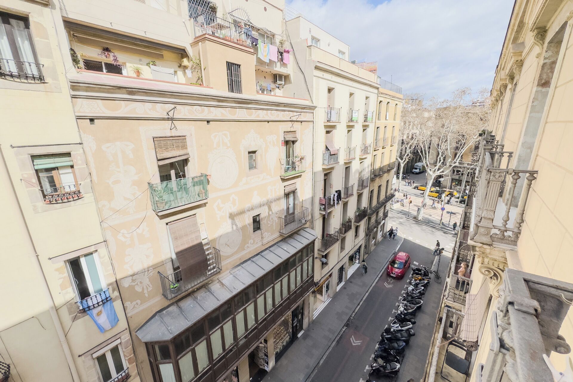 A street view with multi-story buildings, balconies with clothes hanging, and parked scooters.
