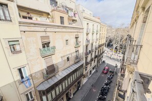 Une vue de rue avec des immeubles à plusieurs étages, des balcons où du linge est étendu, et des scooters garés.
