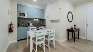 Una cocina compacta con electrodomésticos modernos, una mesa de comedor con sillas y una mesita auxiliar con un farol.
