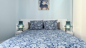 Un dormitorio con una cama, dos mesitas de noche, dos lámparas y una obra de arte en la pared.