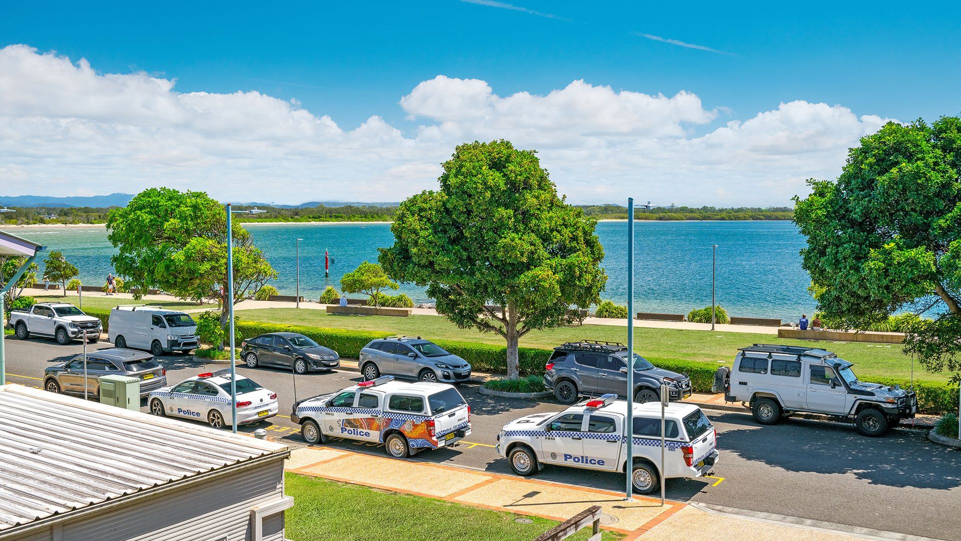 A parking area with police vehicles, a body of water, and trees in the background.