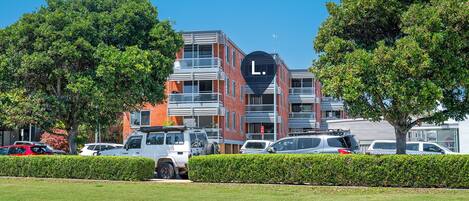 A modern building with a prominent 'L' sign, surrounded by well-maintained hedges and trees.