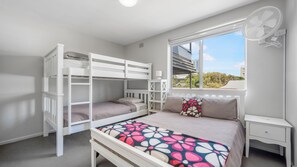 Ein Zimmer mit Etagenbetten, einem Nachttisch, einem Fenster mit Blick und einem Deckenventilator.