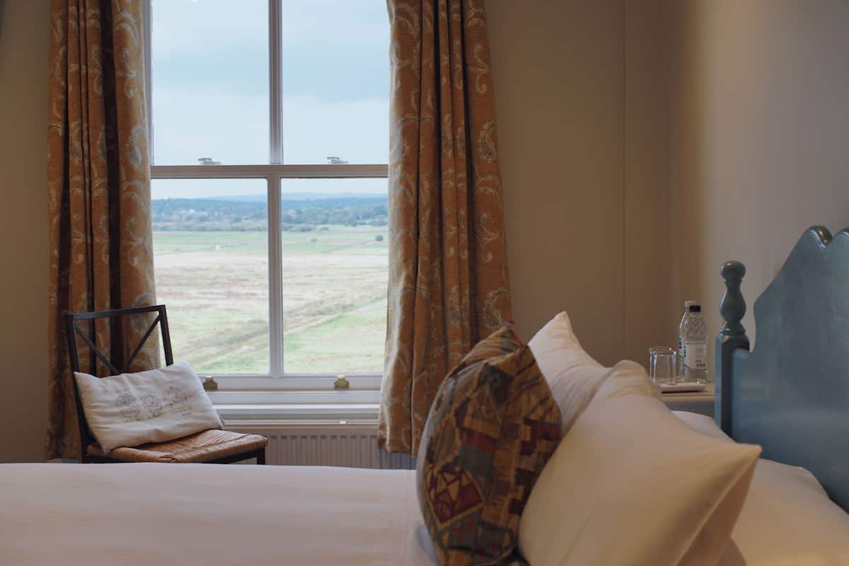 A hotel room with a bed, a chair, a nightstand, and a view of the countryside through a window.
