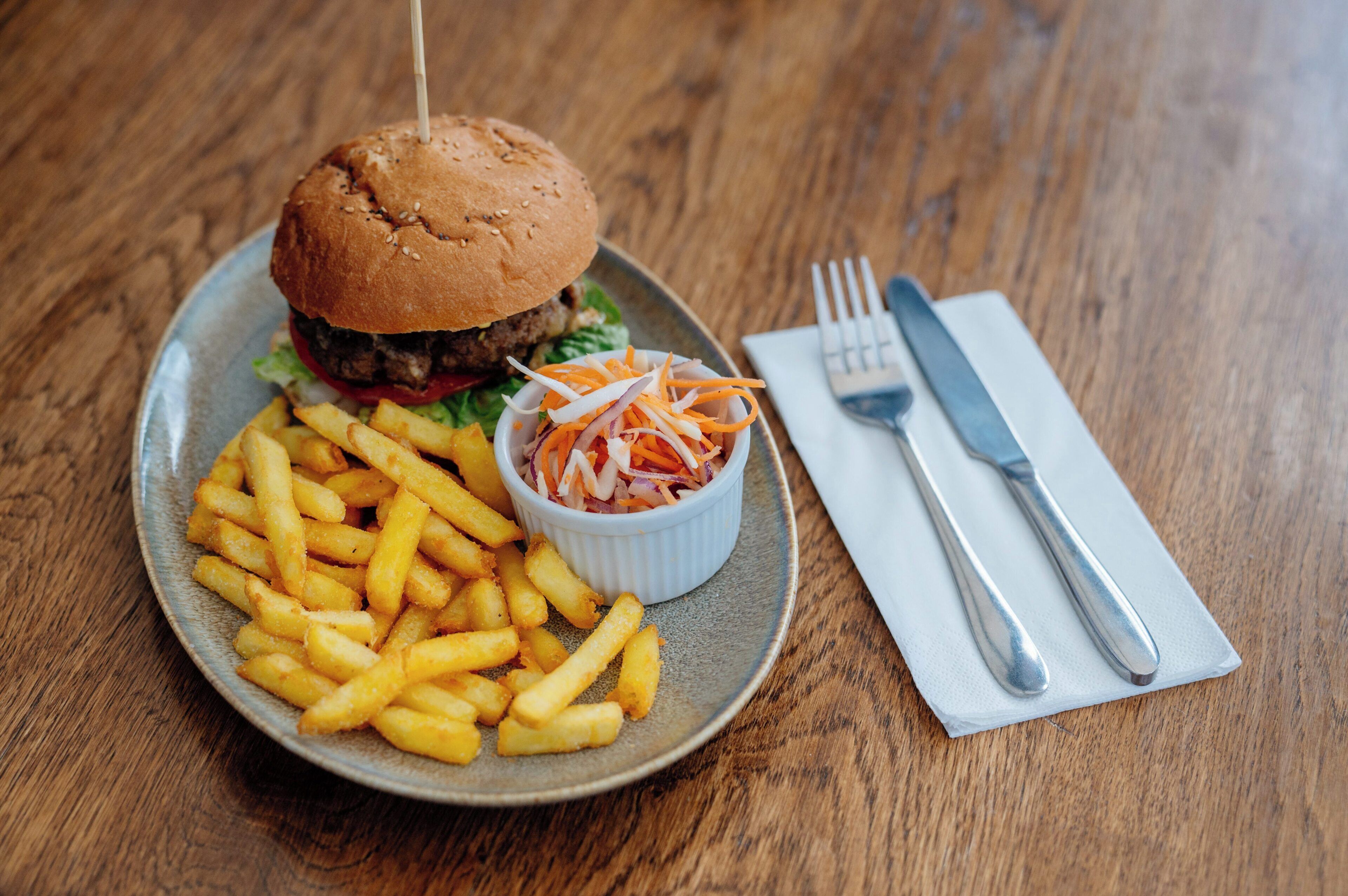 Un plato con una hamburguesa, papas fritas y una ensalada pequeña sobre una mesa de madera.