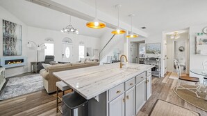 Moderni keittiö, jossa on marmorinen työtaso, valkoiset kaapit ja riippuvalaisimet.