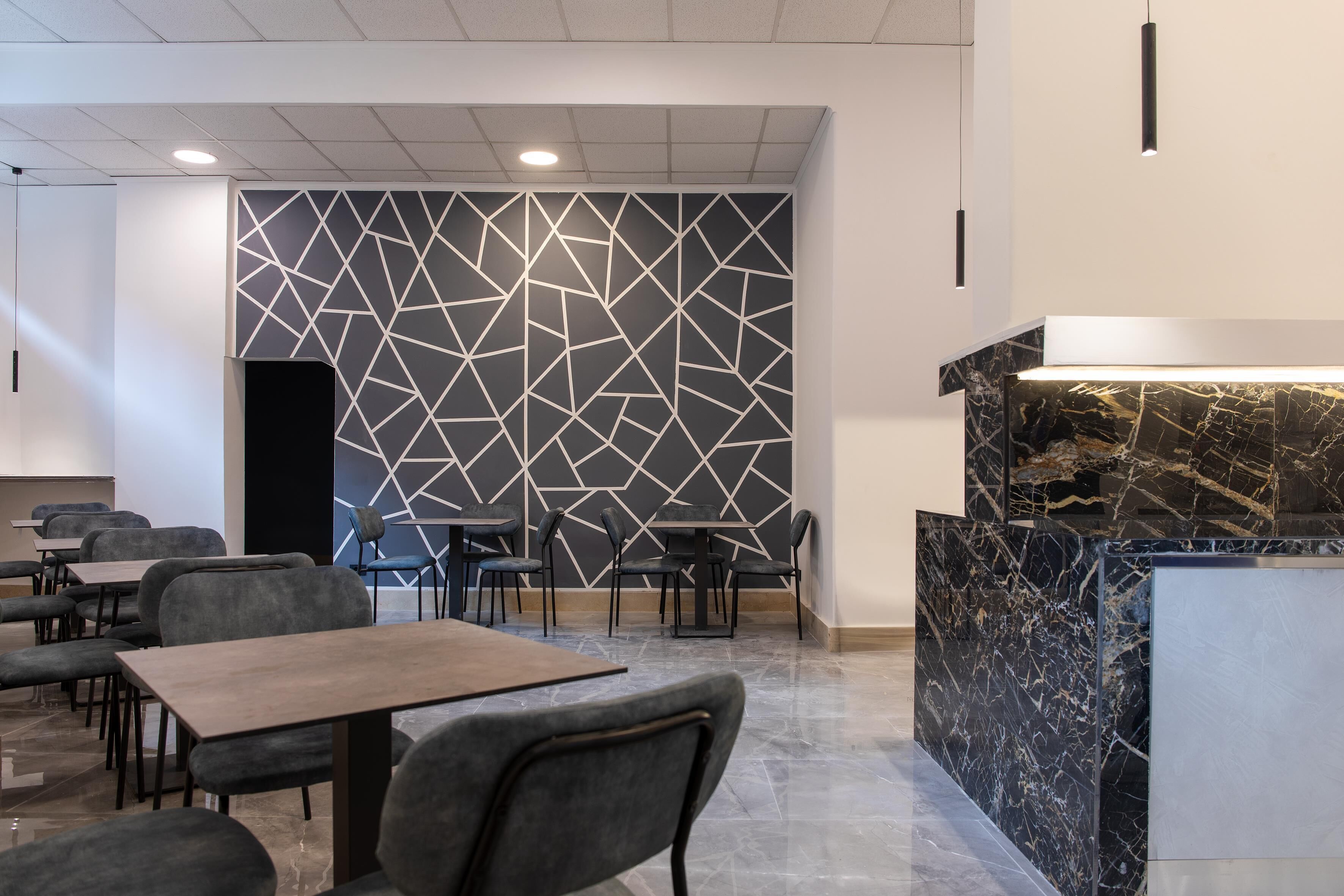 Interno di un ristorante moderno con design geometrico delle pareti, banconi in marmo e diverse tipologie di posti a sedere.