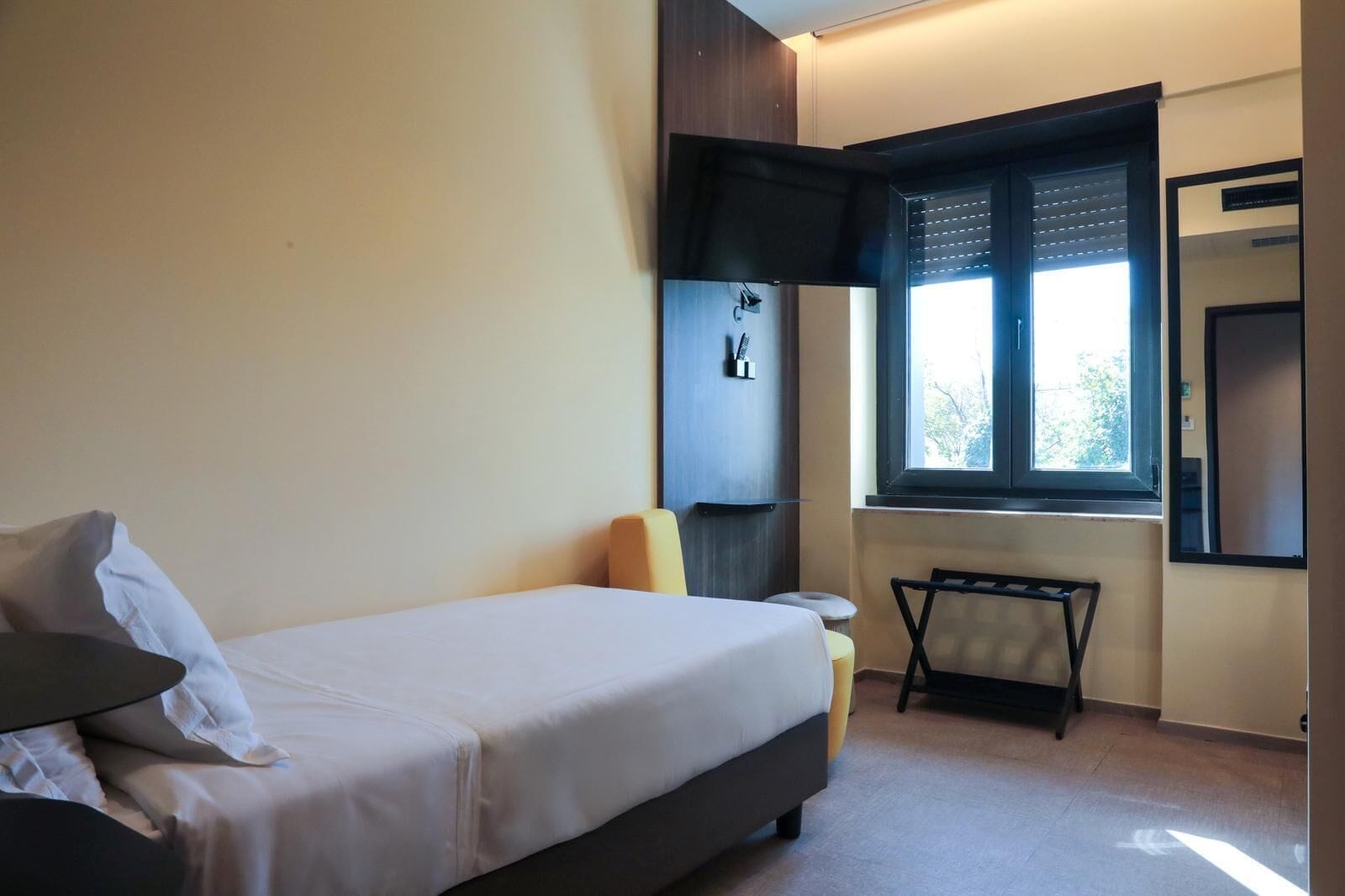 Una camera da letto con un letto, un tavolino, una sedia, una finestra con persiane e uno specchio a parete.