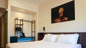 Habitación de hotel con una cama grande, un escritorio con silla, una mesita pequeña y un televisor montado en la pared.