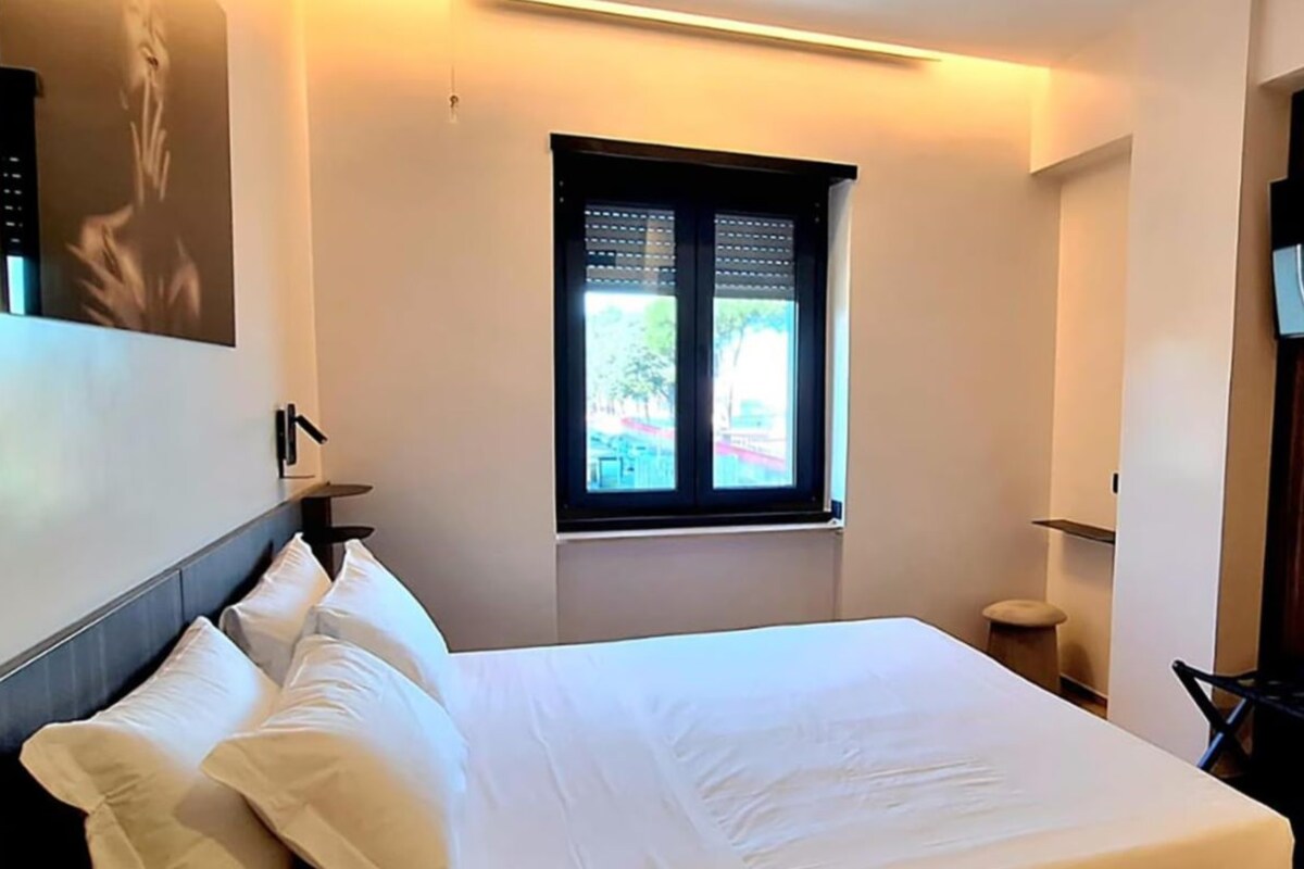 Ein Hotelzimmer mit Bett, Fenster, Tür und einem an der Wand befestigten Fernseher.